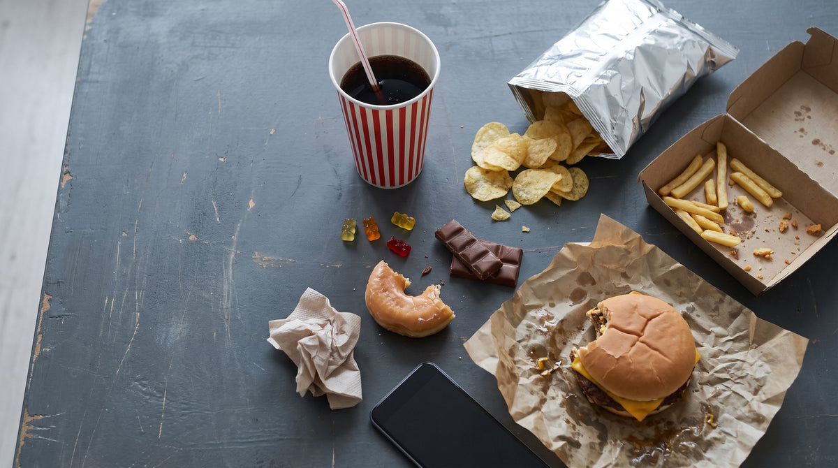Angebissener Burger, Pommes, Cola, Chips, Schokolade und Donut auf einem dunklen Tisch von oben