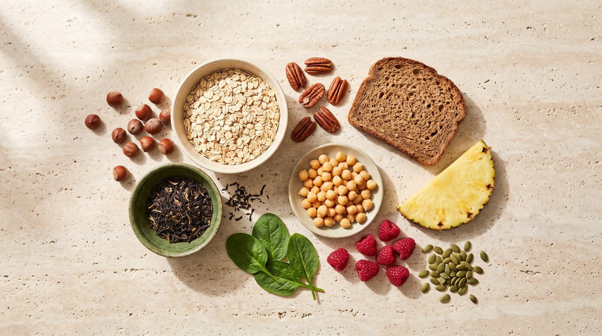 Manganquellen auf hellem Stein: Haferflocken, Haselnüsse, Pekannüsse, Kichererbsen, Vollkornbrot, schwarze Teeblätter, Ananas, Himbeeren, Spinat und Kürbiskerne