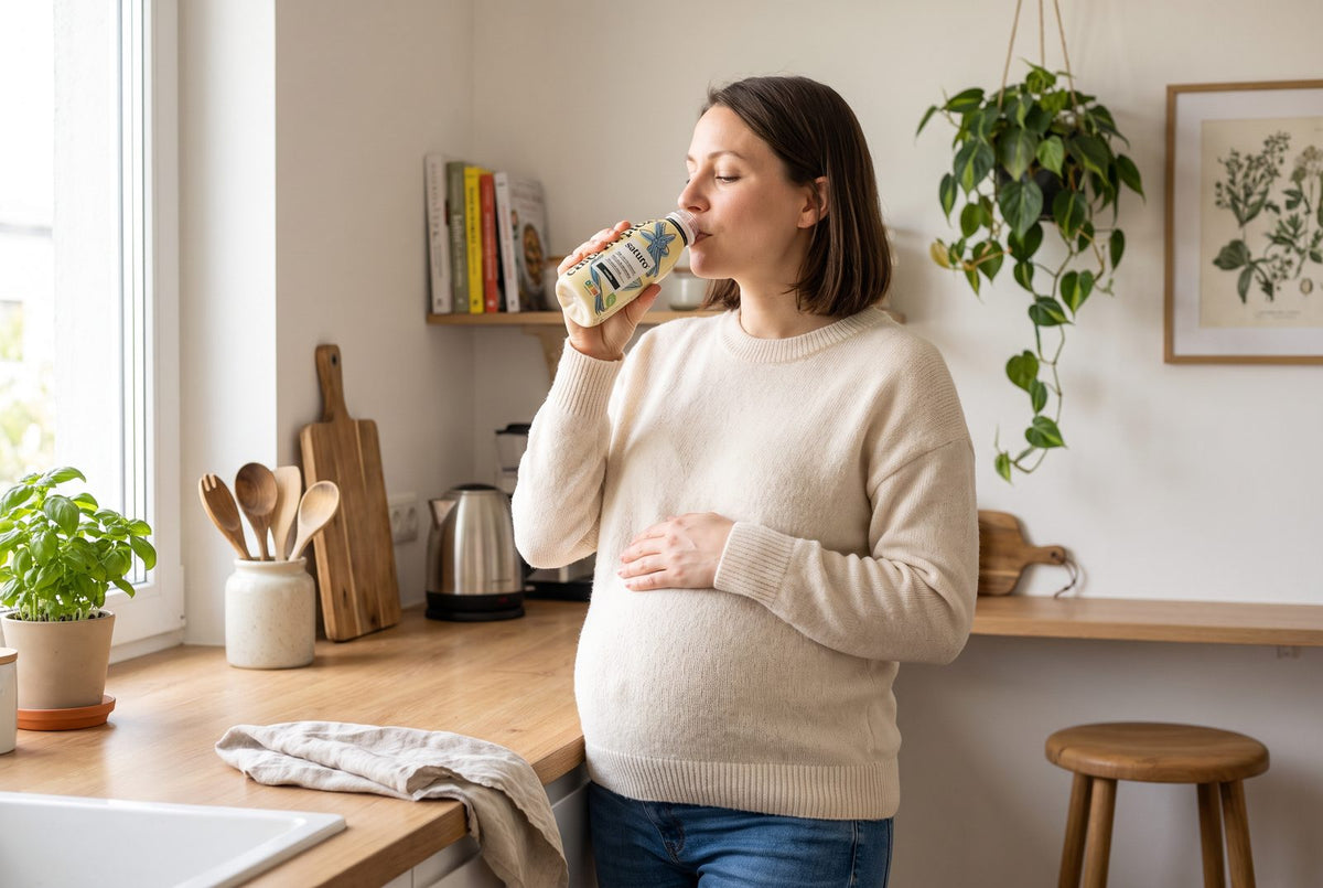 Schwangere trinkt in einer hellen Küche eine Saturo Trinkmahlzeit: In Schwangerschaft und Stillzeit steigt der Vitamin-B2-Bedarf auf 1,3 bis 1,4 mg