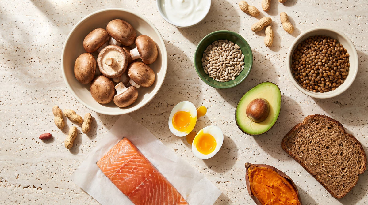 Pantothensäure-Quellen auf hellem Stein: Champignons, Sonnenblumenkerne, Avocado, Eier, Lachs, Linsen, Vollkornbrot, Süßkartoffel und Erdnüsse